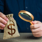 GP stake sales boom raises fund diligence questions A man examines a dollar money bag through a magnifying glass. Investigating capital origins. Anti money laundering, tax evasion. Study terms and conditions on deposit or loan. Find investments
