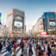 Panorama Shot of People crossing the crowded famous Shibuya Crossing in Downtown Tokyo, illuminated Shibuya Buildings with billboards in the background. Twilight light, close to sunset. Shibuya Crossing, Shibuya Ward, Tokyo, Japan, Asia.