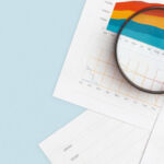 A magnifying glass lies on top of several documents of infographics