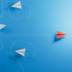 Paper planes, white flying randomlly but for one in red flying with purpose