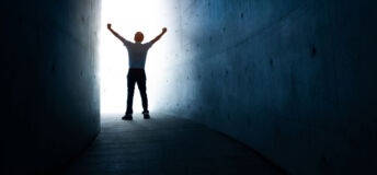 A man standing in the light at the end of a dark tunnel