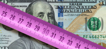 A ten dollar US bill with a ruler on top of it.