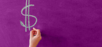 A hand writing a USD sign on a chalkboard