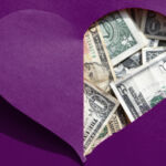 A love-heart shaped hole in a piece of people reveals US dollars underneath