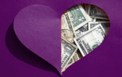 A love-heart shaped hole in a piece of people reveals US dollars underneath