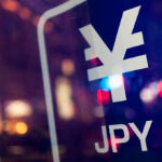 Sign of Japanese yen on a reflective background with street lights blurred in the surface