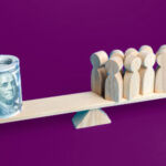 tiny see saw with a roll of dollar bills balancing wooden chess-type pawns