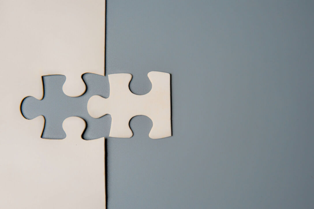 Two puzzle pieces connecting, one white and one grey, on a contrasting background. Two puzzle pieces connecting, one white and one grey, on a contrasting background