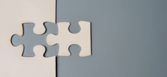 Two puzzle pieces connecting, one white and one grey, on a contrasting background